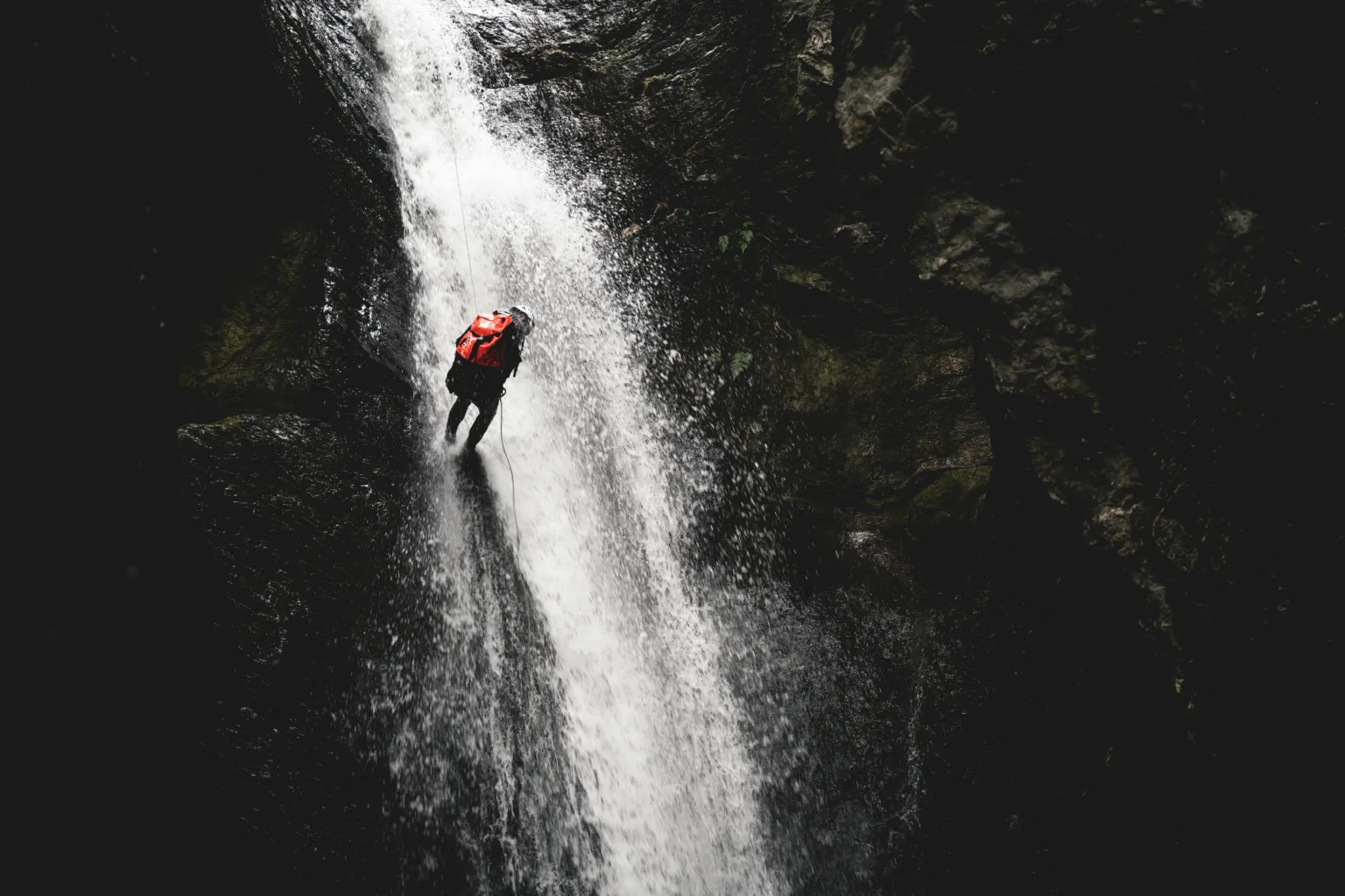 Persona haciendo barranquismo bajo una cascada
